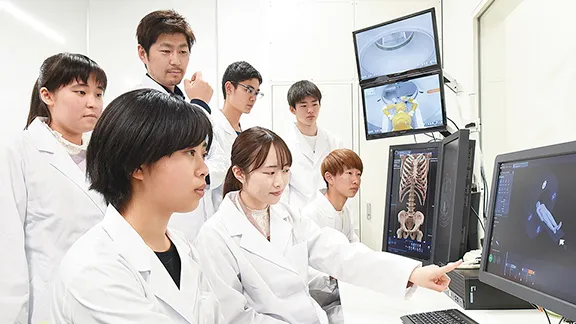 医療技術を学ぶ学生たちがコンピュータ画面を見ながら議論している様子。
