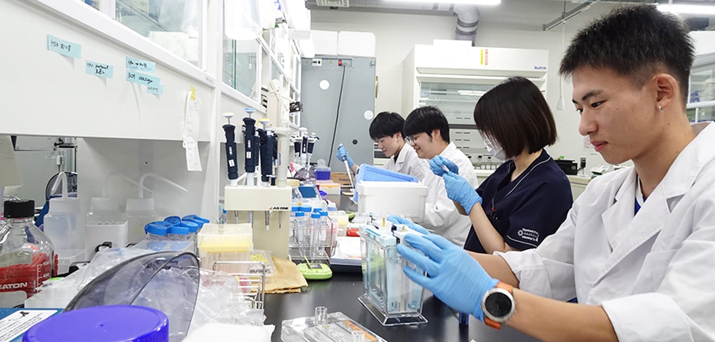 臨床検査室で実験を行う学生たちが、試薬を扱いながら研究に取り組んでいる様子。