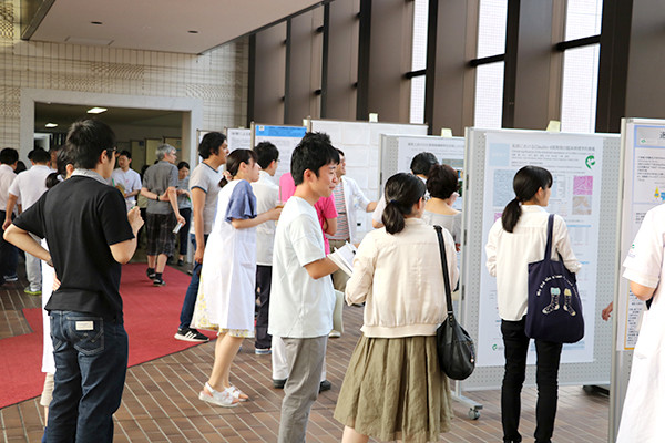 廊下に設置されたポスター前で、大学生や医療関係者が立ち止まり、資料を見たり話し合ったりしている様子。