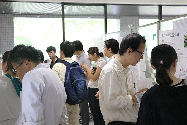 大学内で学生や専門家がポスターを使ってディスカッションする様子。背景には窓があり、外の光が差し込んでいる。