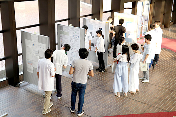 人々が室内でポスター展示を見ながら議論している様子。学生や研究者が情報を共有しています。