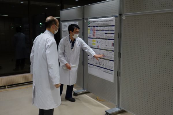 廊下で実施されるポスターセッションに参加する学生や医療関係者たち。研究内容の説明に熱心に耳を傾けている様子。