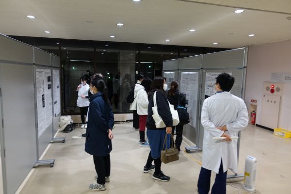 大学内で学生や専門家がポスターを使ってディスカッションする様子。背景には窓があり、外の光が差し込んでいる。