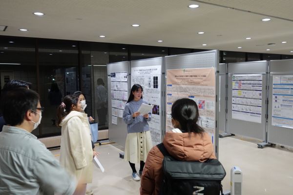 廊下に設置されたポスター前で、大学生や医療関係者が立ち止まり、資料を見たり話し合ったりしている様子。