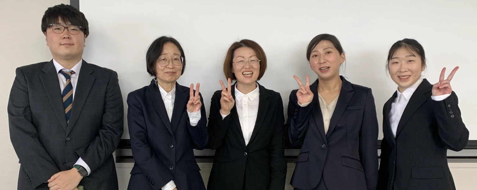 2024年度修士論文発表会に参加した5人の大学院生が、笑顔でポーズをとっている写真。
