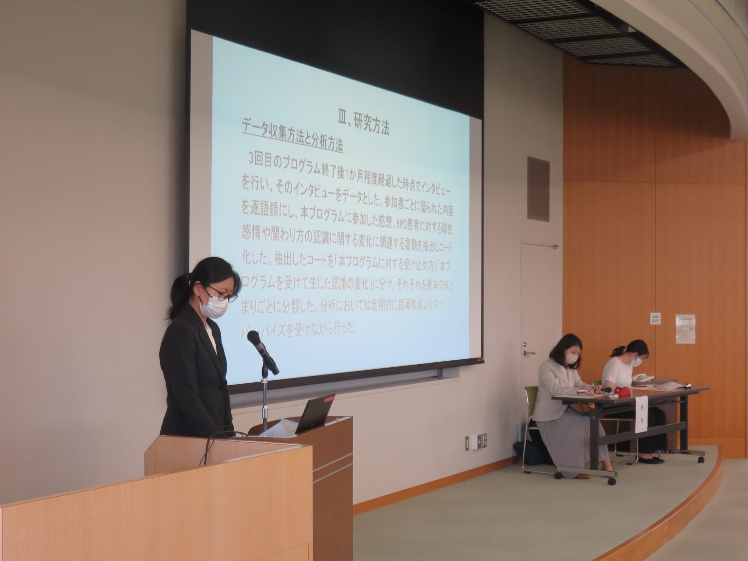 大学院看護学研究科の修士論文研究発表会で発表を行う学生と、資料を確認する聴衆の様子。