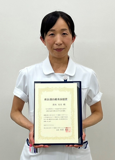 看護学研究科修了生が優秀演題賞を受賞し、賞状を持って微笑む姿。