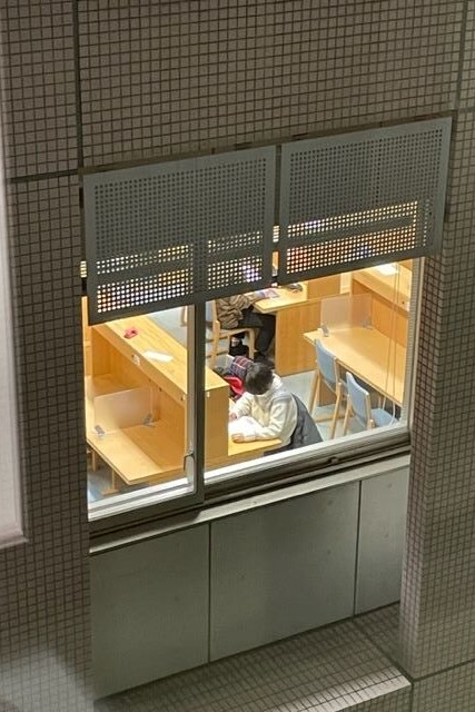 窓越しに見える学習スペースで勉強する学生の姿。
