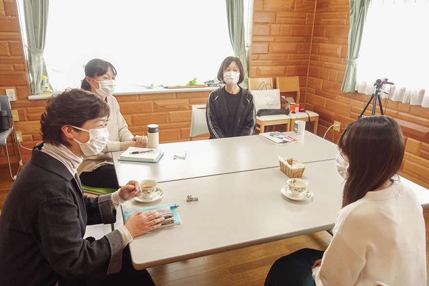 4人のマスクをした人々がテーブルを囲み、メモを取りつつ会話している。