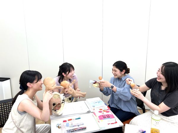 宗像花さんを含む4人の女子大学院生たちが、赤ちゃんの人形を活用し和やかにディスカッションを行う様子。