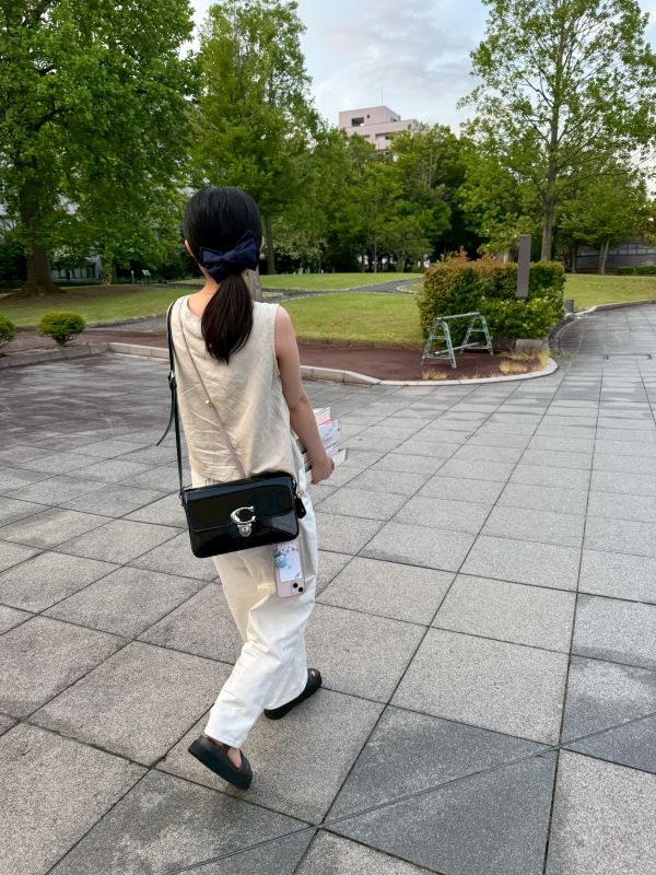 緑に囲まれたキャンパス内で、村田呼春さんが分厚い参考書を運ぶ様子。