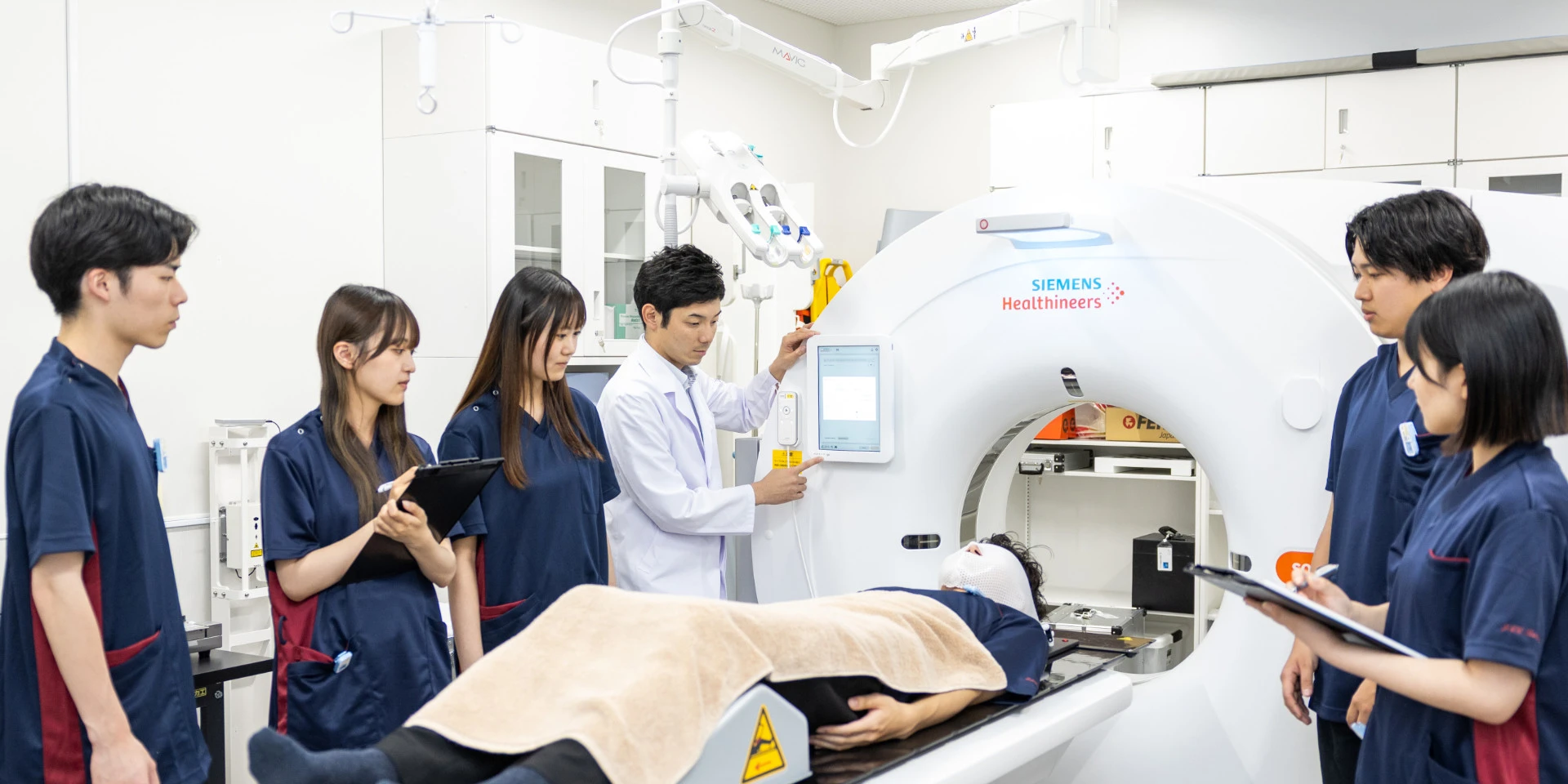 医療実習中の学生たちが、シミュレーターを使ってCTスキャンの手順を学んでいる様子。