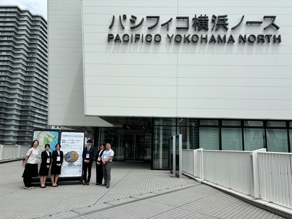 パシフィコ横浜ノースの前で、学会発表を行う学生たちがポスターと共に立っている様子。