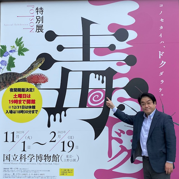 国立科学博物館の特別展「毒」のポスターの前で指を指す男性。展示は動植物や人工毒に関する内容。