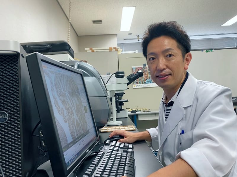 臨床検査技師が顕微鏡の前で病理検査のデータを分析している様子。