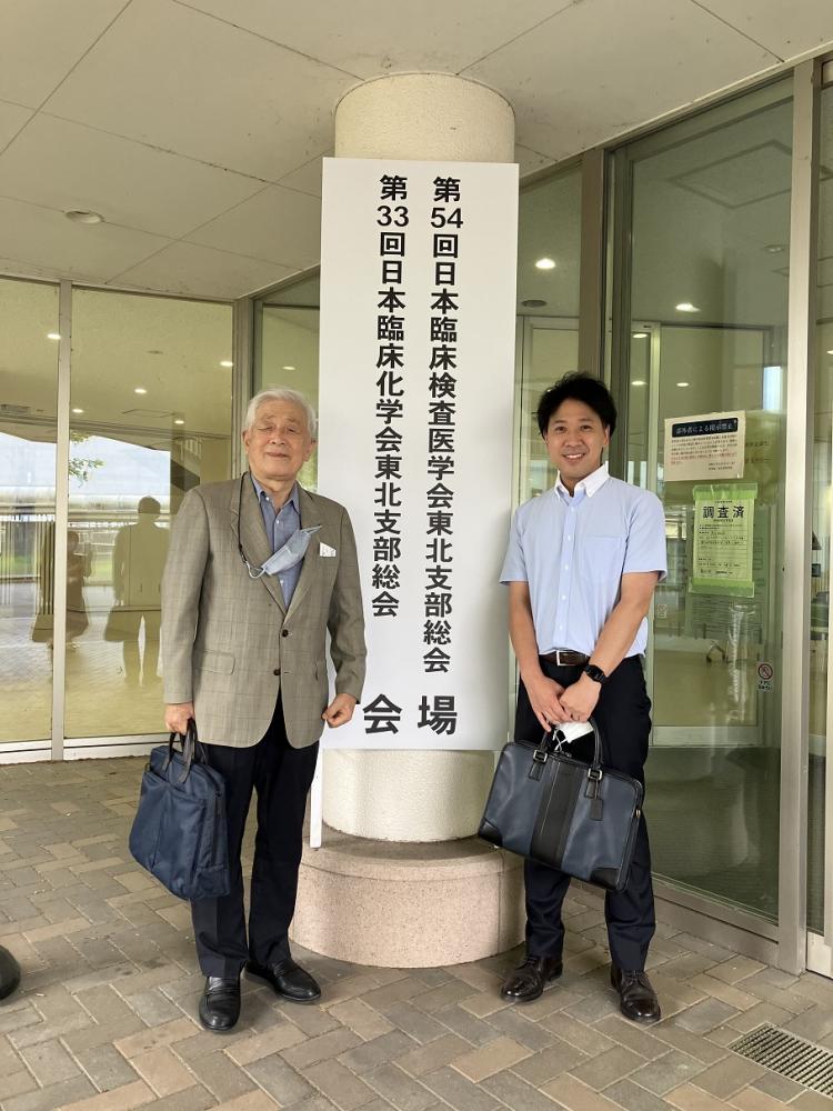 東北大学で開催された学会の前で、講師と学生が並んで立っている写真。
