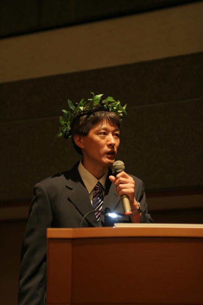 学会で月桂冠をつけて発表する男性の姿。シンポジウムのテーマに合わせたユニークな演出。