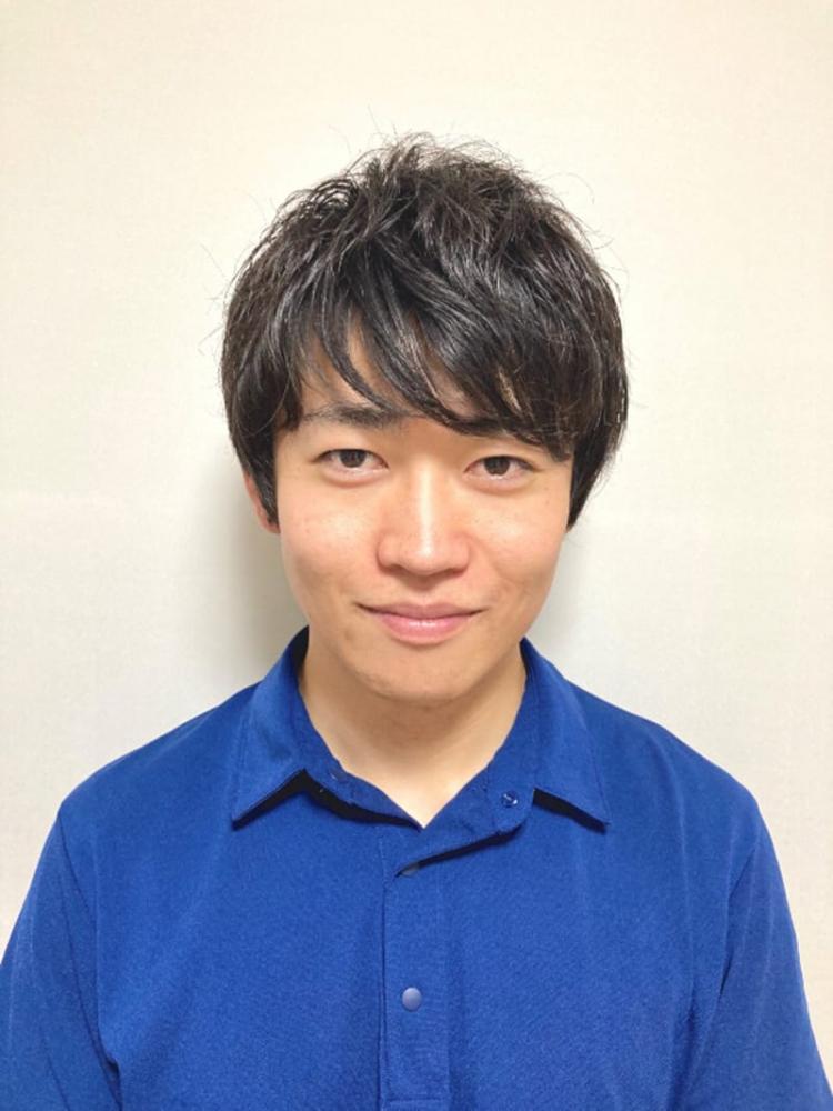 大学の英語教育を担当する男性が青いシャツを着て微笑んでいるポートレート。