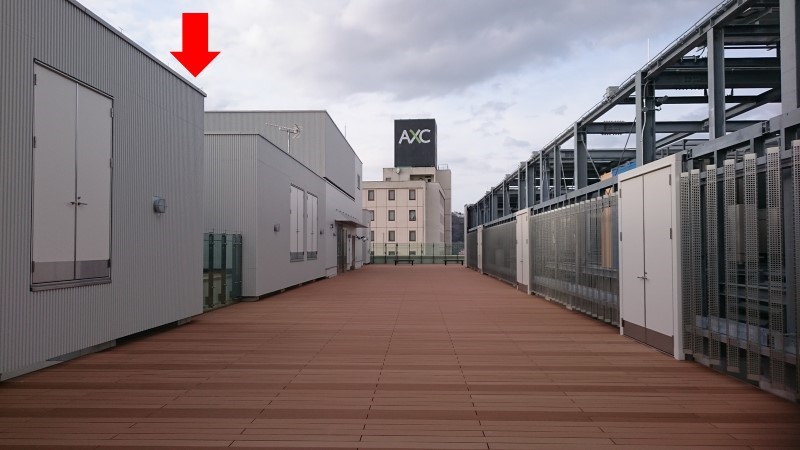 福島駅前キャンパス屋上の観測機材設置場所を示す画像。木製デッキと周囲の建物が見える。