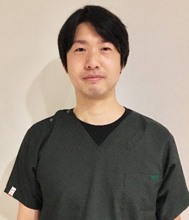 作業療法士の男性が黒いTシャツと作業着を着て、カメラに向かって微笑んでいるポートレート。