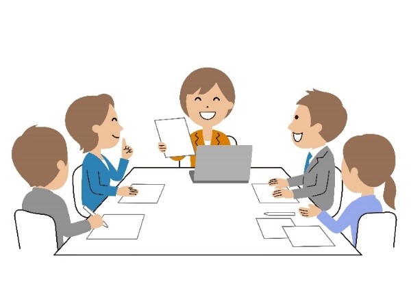 職場でのグループディスカッションを行う人々、中央の人物が資料を持って笑顔で話している様子。