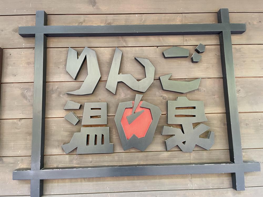 りんご温泉の看板が掲げられた木製の壁。温泉の名前が特徴的なデザインで表現されている。