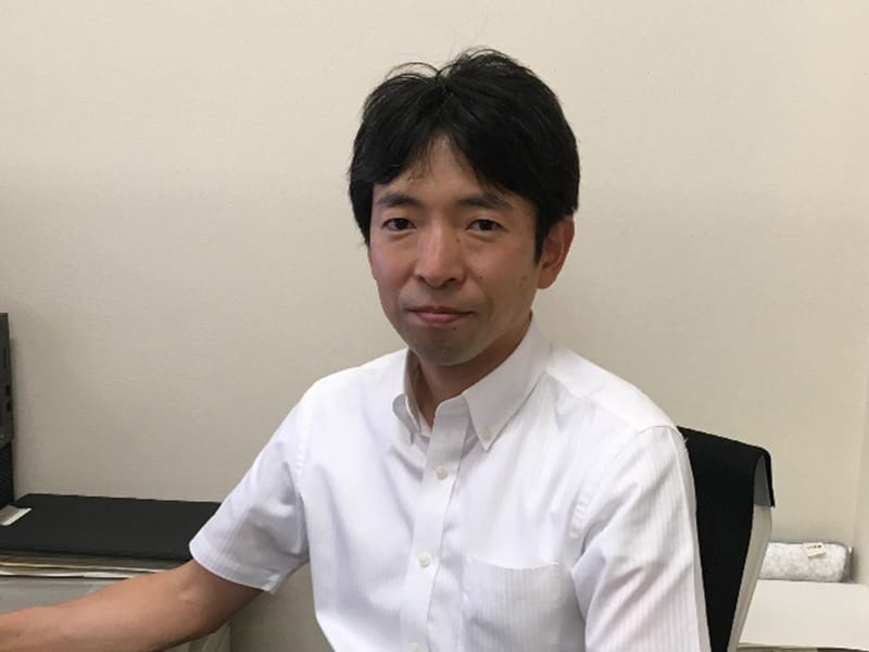 作業療法士として活動する男性が、オフィスで微笑みながら座っている様子。