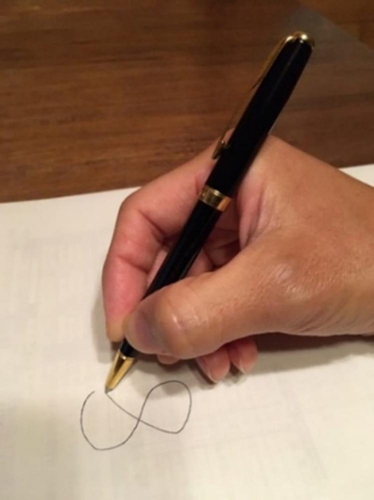手にペンを持ち、紙に文字を書こうとしている様子。手の動きと感覚が作業に与える影響を示唆。