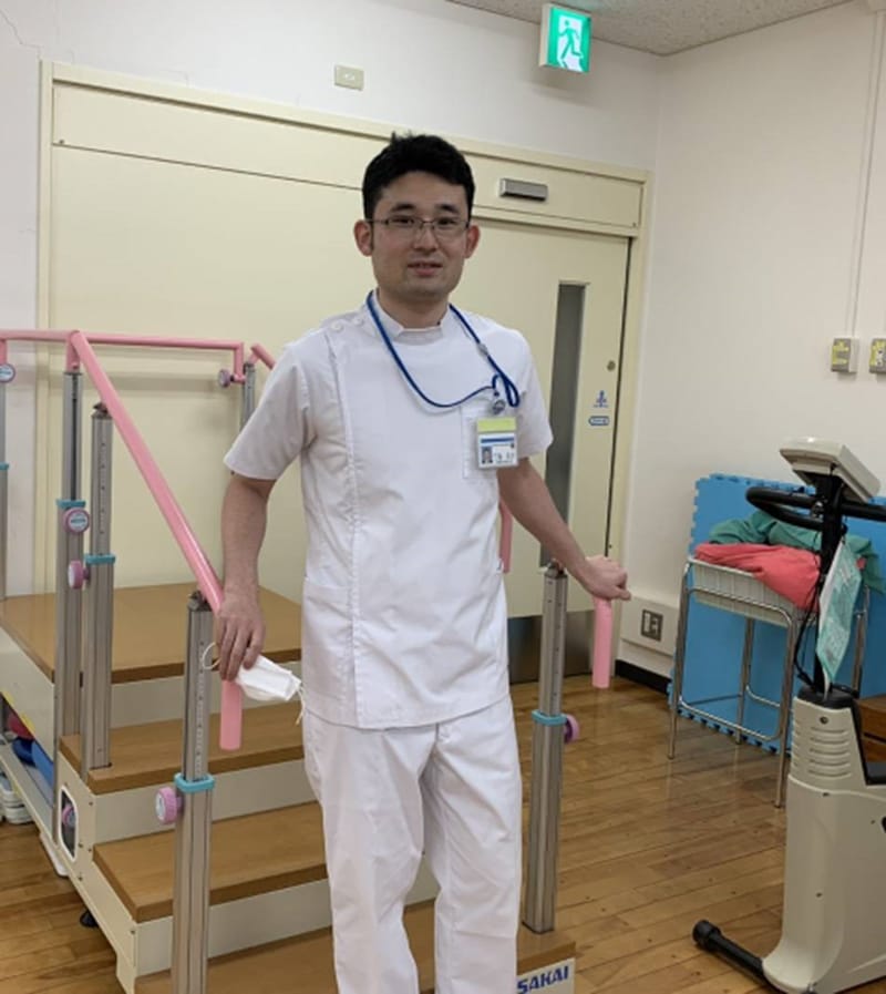 作業療法士の男性がリハビリテーション用の器具の前に立っている様子。