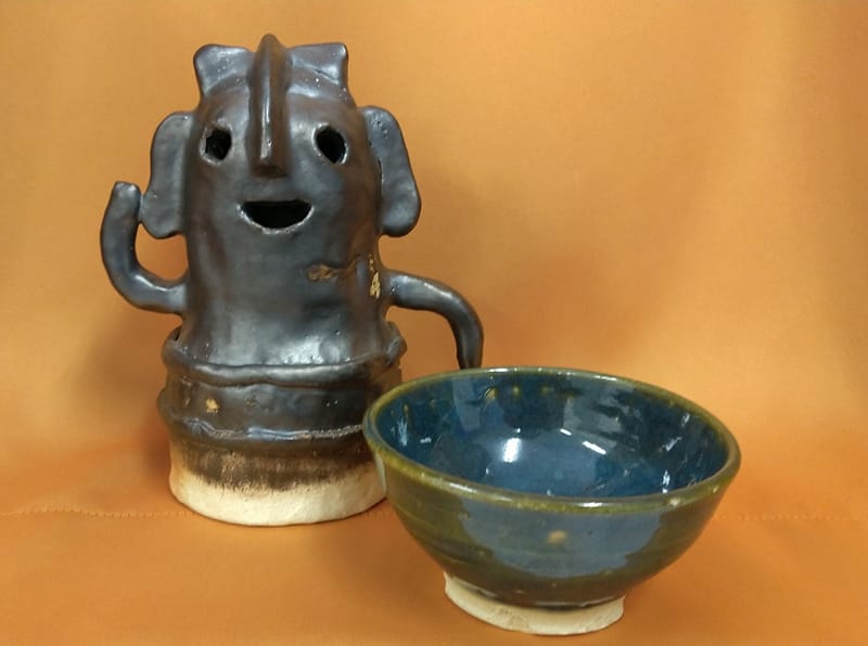 陶芸作品の笑顔のキャラクターと青い陶器のボウルが並んでいる画像。