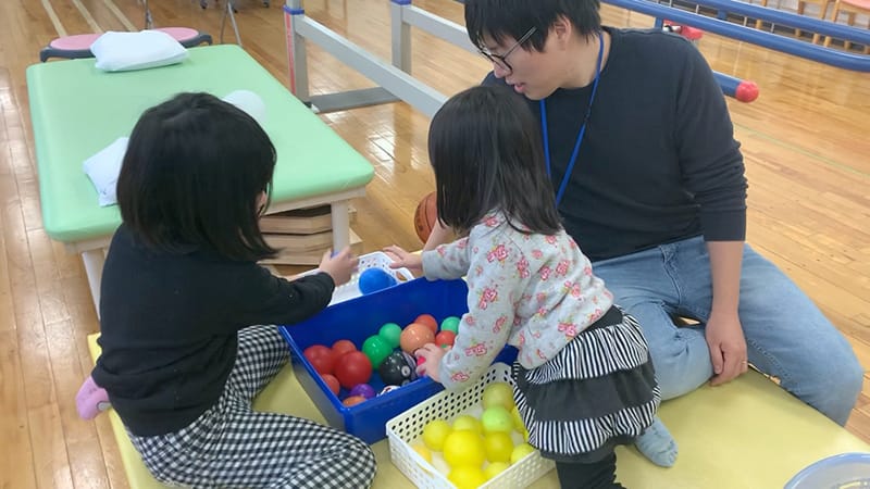 子どもたちがカラフルなボールで遊びながら、作業療法士と一緒に楽しんでいる様子。