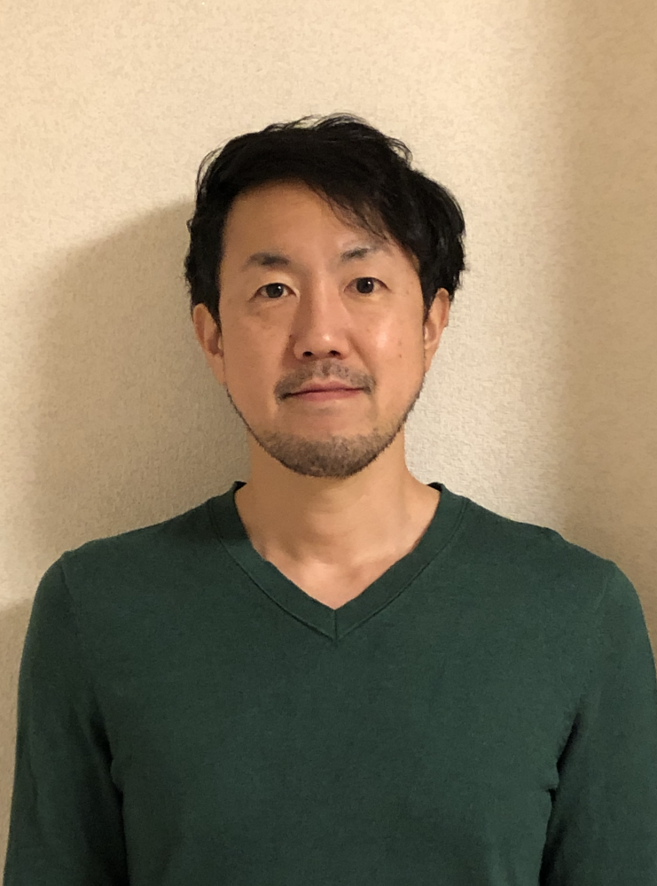 緑の服を着た阿部浩明さんがカメラに向かって微笑んでいるポートレート。