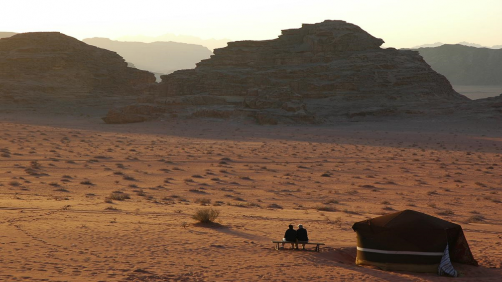 砂漠の夕暮れ時、テントの近くで座る二人の人物が見える風景。