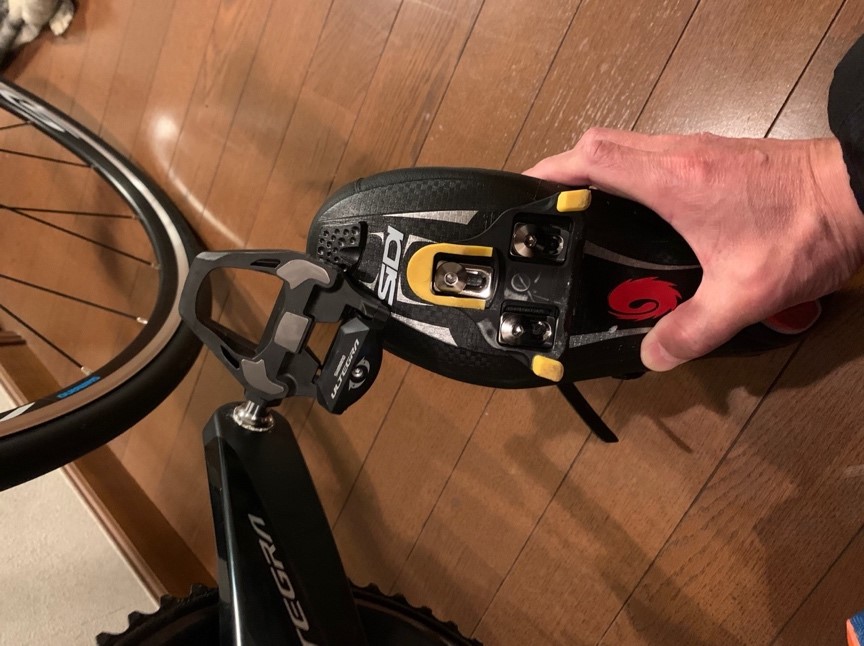 ビンディングペダルと靴を手に持ち、自転車の準備をしている様子。