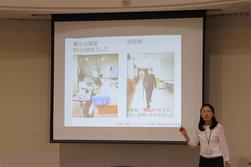 理学療法士がプレゼンテーションを行い、スライドに治療室の写真を示している様子。