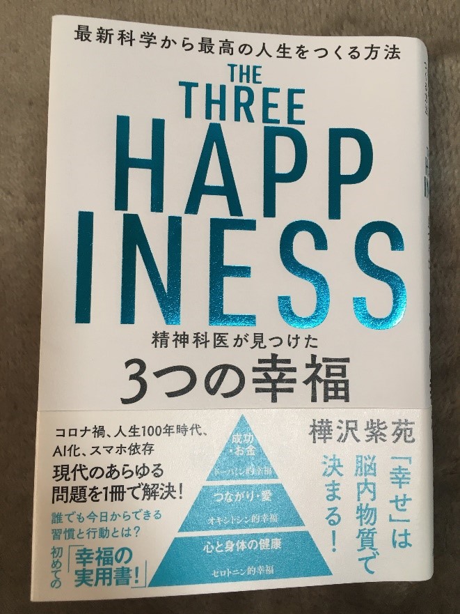 「3つの幸福」をテーマにした書籍の表紙、青い文字でタイトルが印刷されている。