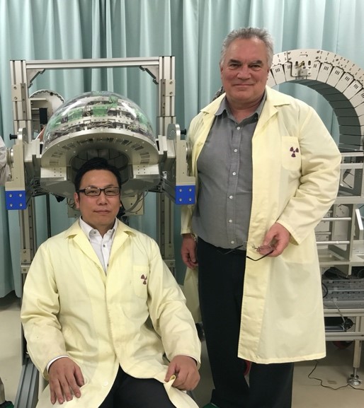 ヘルメットPET装置の前で、研究者とPaul E. Kinahan教授が白衣を着てポーズを取っている写真。