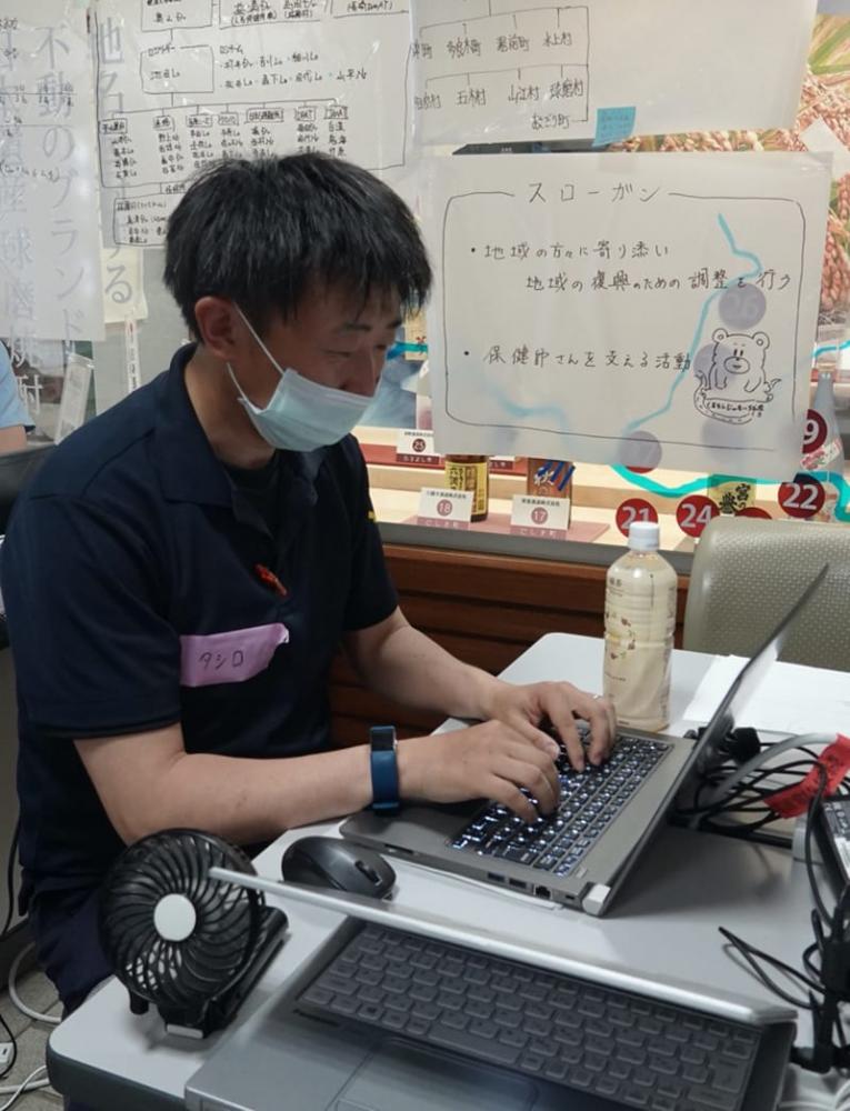 支援活動中の男性がパソコンで作業している様子。周囲にはメモや飲み物が置かれている。
