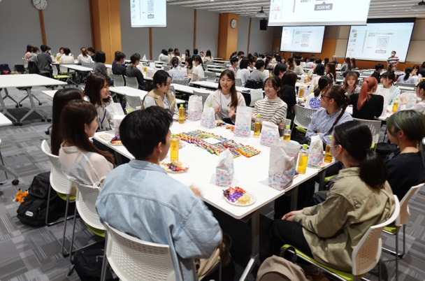 臨床検査学科の学生交流会で、テーブルを囲んで話し合う学生たちの様子。飲み物やお菓子が並んでいる。