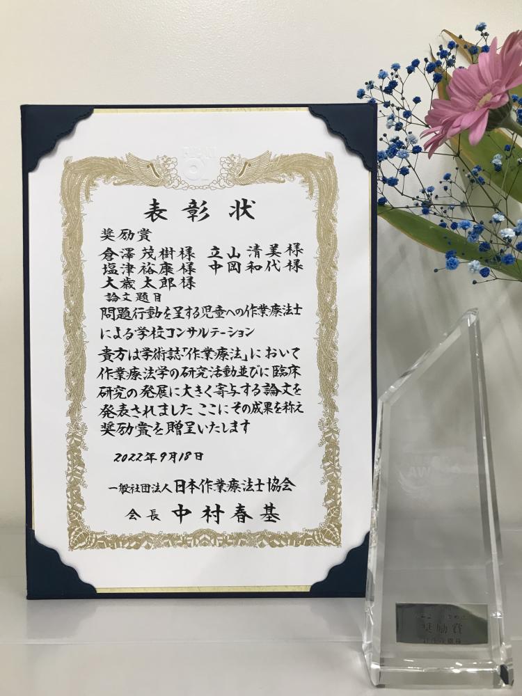 作業療法学科の教員が日本OT協会論文賞を受賞したことを示す表彰状とトロフィーの画像。