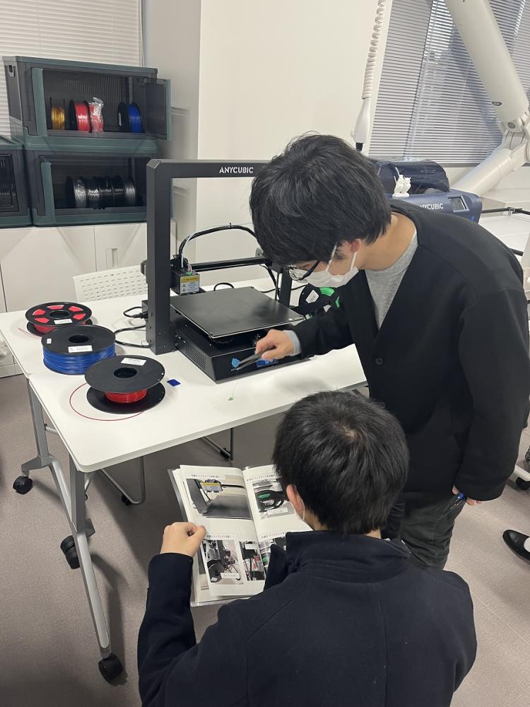 3Dプリンタ体験会で機械を操作する参加者たちが、プリントの手順を確認している様子。