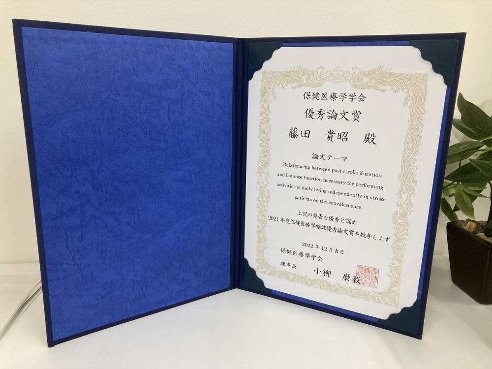 作業療法学科の藤田准教授が受賞した優秀論文賞の証書が開かれた状態で写っている画像。