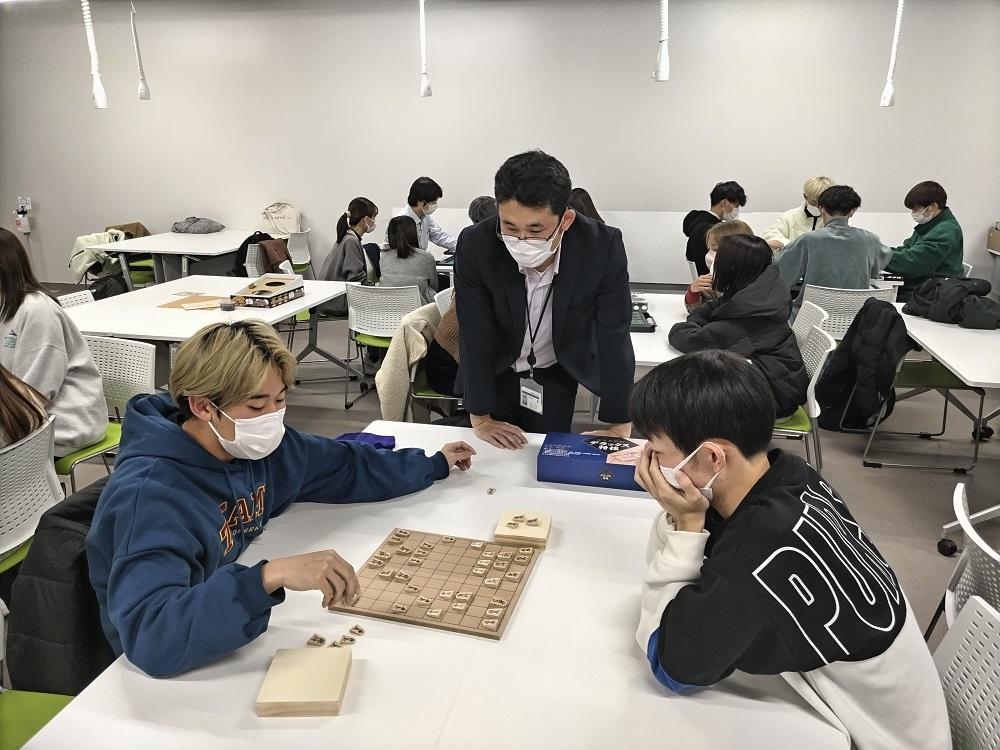 第5回おきゅらぼで、参加者がボードゲームを楽しんでいる様子。テーブルにはゲーム盤と駒が置かれ、周囲には他の参加者もいる。
