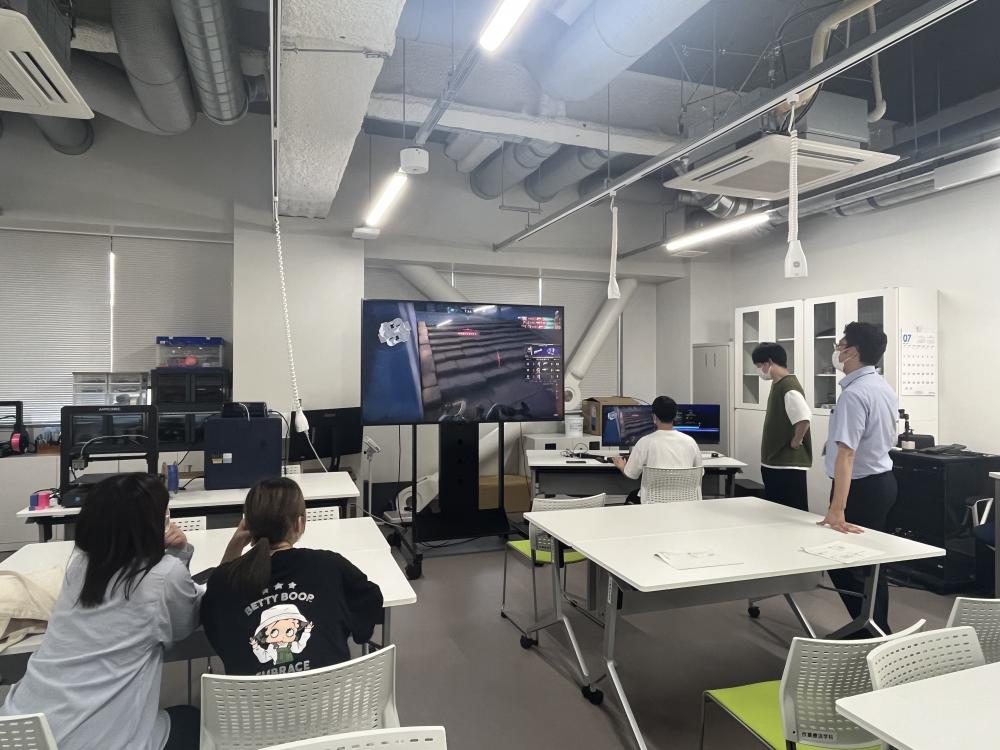 作業療法の講義中、学生たちがe-sportsのプレイ体験を楽しんでいる様子。大画面でゲームが映し出され、参加者が熱心に見守る。