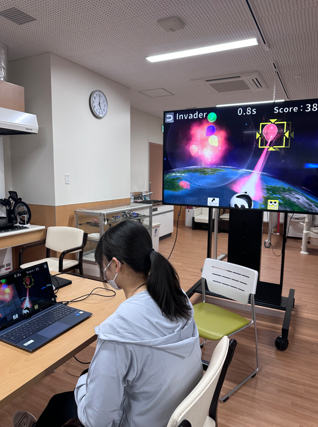 医療関連のゲームをプレイする学生が、モニターでスコアを確認している様子。