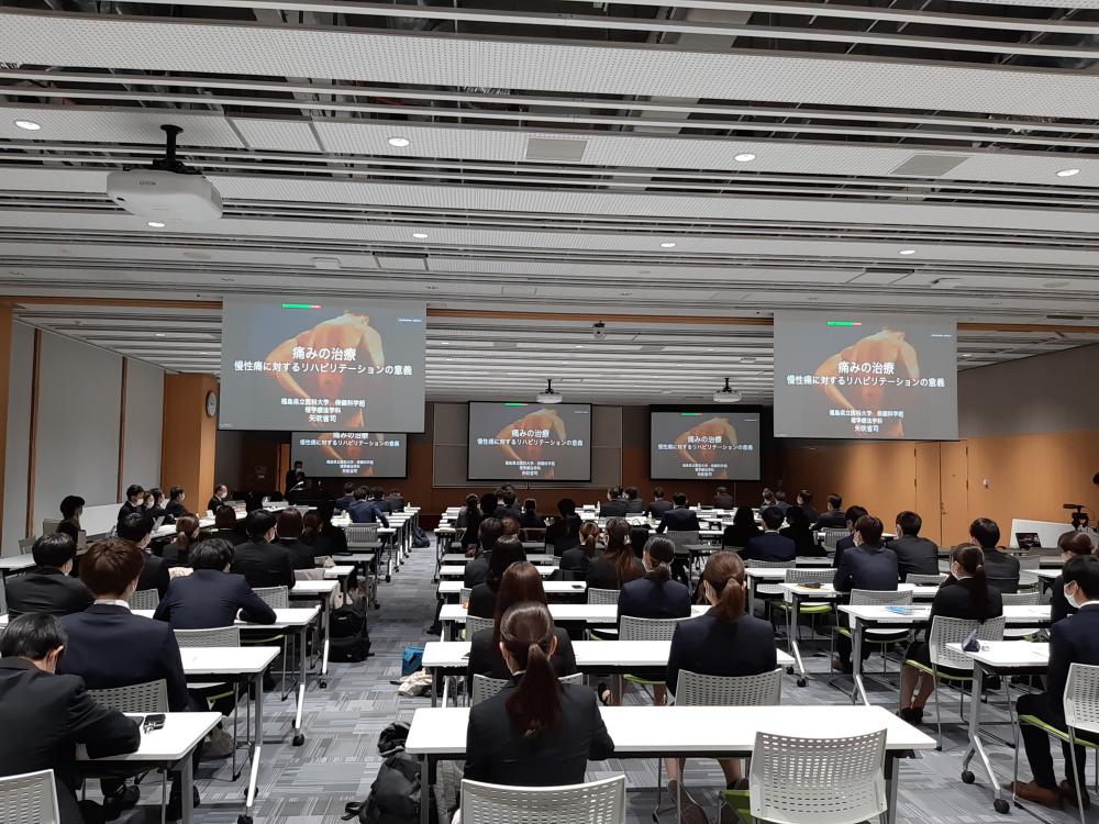 臨床実習説明会の様子。多くの学生が参加し、スクリーンに映る講演内容を注視している。