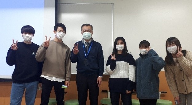 教員と学生がマスクを着用し、交流会でポーズをとっている様子。
