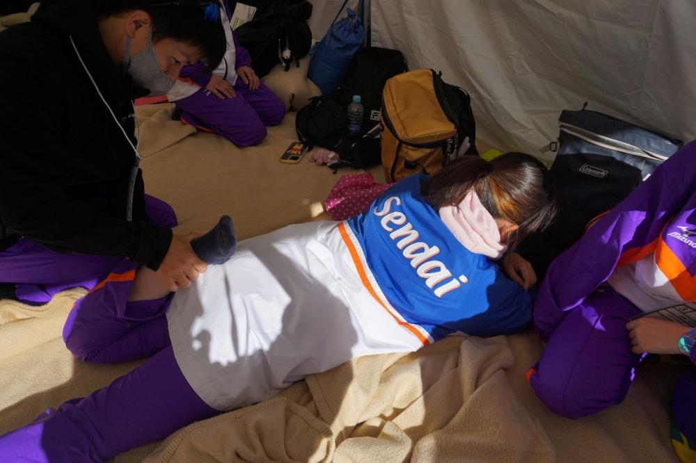 障がい者スポーツ大会で、選手がマッサージを受けている様子。周囲には他の選手やスタッフがいる。
