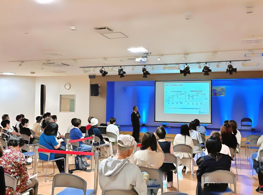 理学療法学科の教員が講演を行い、参加者が聴講している様子。背景にはプレゼンテーション用のスクリーンが設置されている。