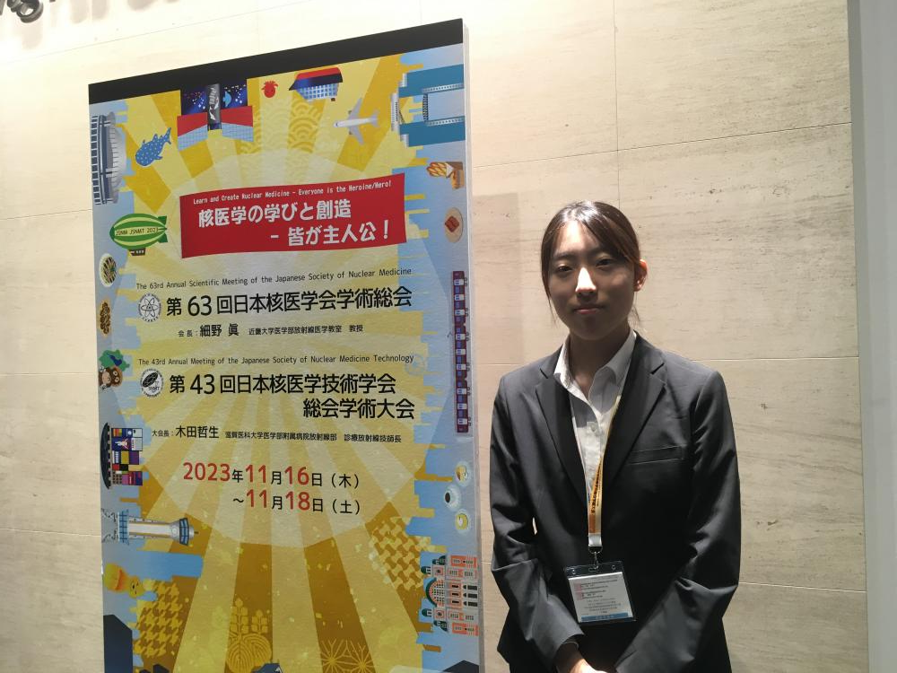 診療放射線科学科の学生が学会発表のポスターの前で立っている様子。